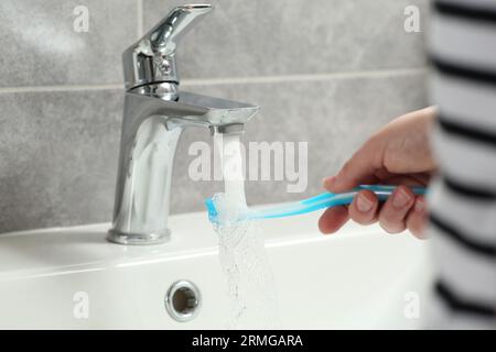 Femme lavant la brosse à dents en plastique sous l'eau qui coule du robinet dans la salle de bain, closeup Banque D'Images