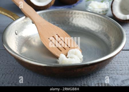 Poêle à frire avec huile de cuisson de noix de coco bio et spatule sur table en bois gris, gros plan Banque D'Images