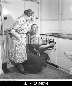 Dans les années 1950 Un homme de la cuisinière électrique nouvellement installée du fabricant suédois Husqvarna, démontre ses caractéristiques. Une femme se tient debout sur le côté regardant. Suède 1950. Kristoffersson réf AZ69-11 Banque D'Images