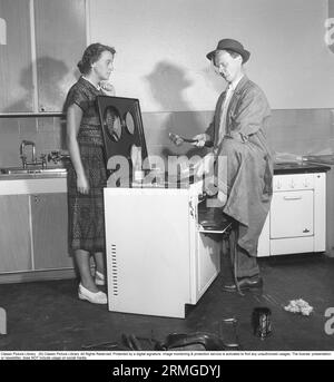 Dans les années 1950 Un homme à une cuisinière électrique du fabricant suédois Husqvarna, faisant un peu de travail sur le poêle à l'air très non-professionnel.Une femme est debout sur le côté le regardant dans un manoir sceptique. Suède 1950. Kristoffersson réf AZ69-12 Banque D'Images