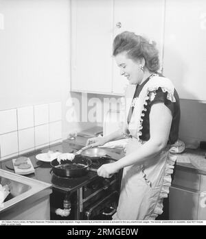 Dans la cuisine 1940s. Intérieur d'une cuisine et une jeune femme debout à la cuisinière de cuisine frire des œufs dans la poêle. Elle porte un tablier. Suède 1947. Kristoffersson réf. AB3-2 Banque D'Images