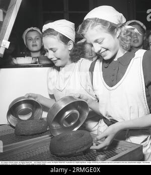 Les deux jeunes adolescentes Inga-Lisa Larsson et Maj-Britt Nilsson, vêtues de tabliers et de foulards, ont fini de cuire leurs biscuits au sucre et les sortent maintenant des moules, et les deux filles semblent avoir réussi avec leurs gâteaux. En arrière-plan, d'autres filles se tiennent debout et regardent. Les filles suivent un cours de pâtisserie à Eskilstuna. Suède 1943. Kristoffersson réf. B119-5 Banque D'Images