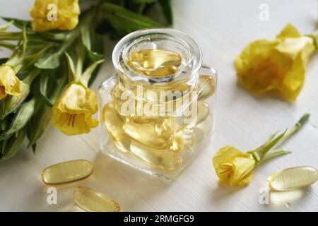 Capsules de gel d'huile d'onagre avec des fleurs d'Oenothera biennis sur une table blanche Banque D'Images