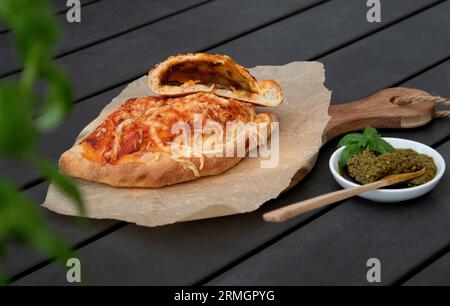 Pizza calzone découpée avec sauce tomate, pesto vert et fromage sur assiette en bois Banque D'Images
