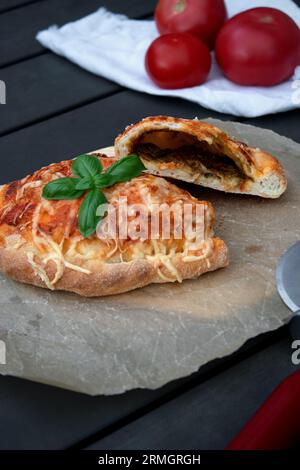 Pizza calzone découpée avec sauce tomate, pesto vert et fromage sur assiette en bois Banque D'Images
