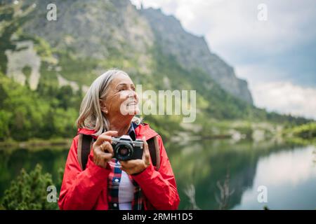 Potrait de femme senior active sur la randonnée dans les montagnes d'automne prenant des photos avec l'appareil photo. Banque D'Images