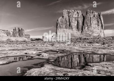 Image numérique en noir et blanc des tours de palais de justice et des trois commérages reflétés dans des piscines temporaires de slickrock dans le parc national des Arches. Banque D'Images