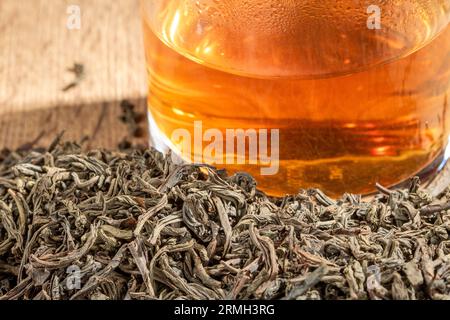 Un verre de thé frais se dresse au milieu d'une pile de thé sec en gros plan. Banque D'Images