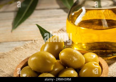 Un bouquet d'olives vertes et un pichet d'huile d'olive sur une serviette en toile de jute, style rustique. Banque D'Images