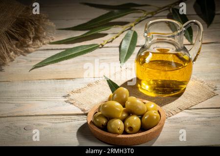 Un bouquet d'olives vertes et un pichet d'huile d'olive sur une serviette en toile de jute, style rustique. Banque D'Images