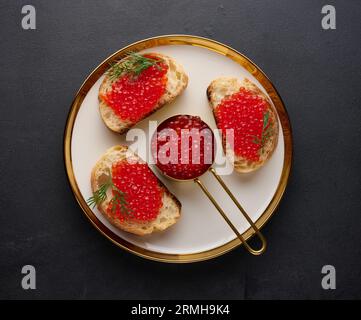 Sandwichs au caviar rouge et au pain dans une assiette ronde sur une table noire, vue de dessus Banque D'Images