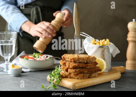 Savoureux schnitzels servis avec couteau, frites et femme cuisinant salade à la table grise, gros plan Banque D'Images