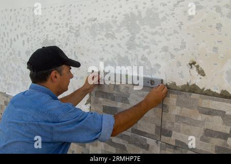 Image d'un carreleur qui utilise un niveau à bulle pour vérifier et s'assurer que les carreaux sont posés correctement. Travaux de restauration à faire soi-même. Banque D'Images