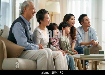 famille asiatique de trois générations assis sur le canapé à la maison regardant la télévision ensemble heureux et souriant Banque D'Images