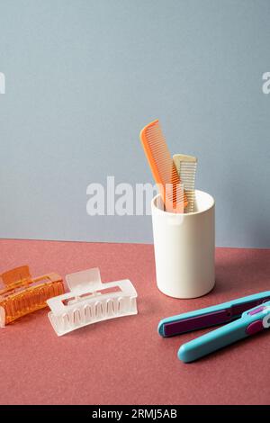 Outil pour coiffer. Brosse à cheveux et épingle à cheveux, fer à lisser sur la table rouge. fond de mur gris Banque D'Images