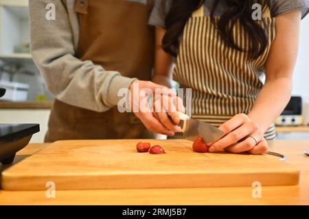 Cliché recadré de jeunes couples coupant des fraises sur le comptoir de cuisine, préparant un petit déjeuner sain ensemble Banque D'Images