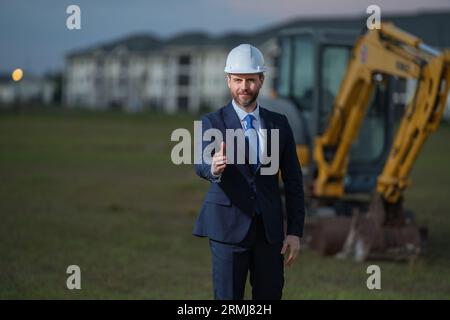 Directeur de construction en costume et casque sur un chantier de construction. Un employé ou un superviseur du directeur de la construction portant un casque de sécurité devant la maison Banque D'Images