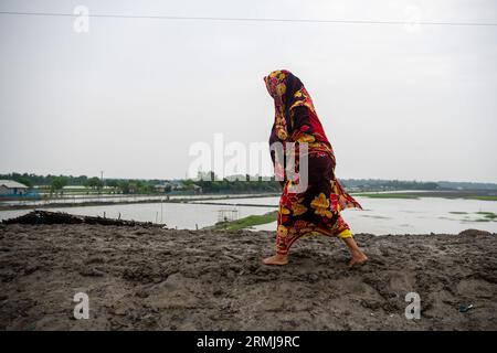 26 août 2023, Khulna, Bangladesh : une femme vue marchant le long d'un barrage de rivière boueux endommagé après de fortes pluies à Kalabogi dans Khulna. Il n'y a pas si longtemps, Kalabogi, un village côtier du Bangladesh, était plein de terres cultivables jusqu'à ce que la montée du niveau de la mer commence à envahir la région jusqu'au golfe du Bengale. De fréquents cyclones et inondations frappent le village depuis la fin des années 1990 En 2009, un cyclone majeur nommé Aila a détruit les 1 400 kilomètres de remblais du pays, 8 800 kilomètres de routes et environ 3 50 000 acres de terres agricoles. Plusieurs centaines de personnes auraient été tuées dans le dis Banque D'Images