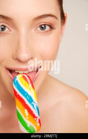 Jeune femme souriant et mangeant du popsicle multicolore glacé Banque D'Images