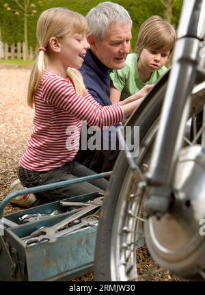 Petits-enfants aider grand-père la réparation de moto Banque D'Images