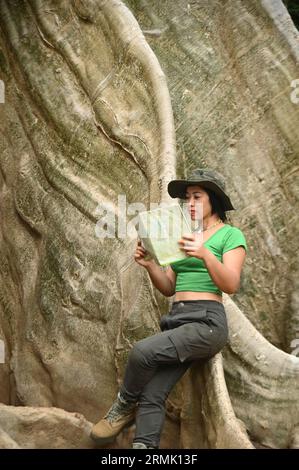 Jolie femme asiatique regardant une carte aux racines d'un grand arbre cet arbre est très grand et est une attraction populaire pour les touristes thaïlandais. À Uthai Thani ville. Banque D'Images