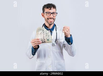 Jeune médecin souriant tenant l'argent isolé. Joyeux docteur tenant des billets de dollars isolés Banque D'Images