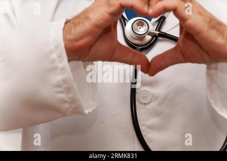 Gros plan des mains d'un médecin donnant la forme d'un cœur avec un stéthoscope en arrière-plan Banque D'Images