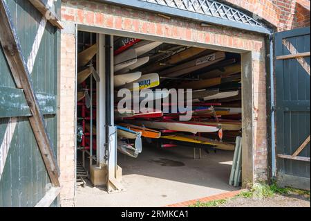 Vu à travers les portes ouvertes, une variété de canoës, kayaks et écules d'aviron entreposés dans le hall à bateaux du Richmond Canoe Club. Richmond, Londres, Angleterre, Royaume-Uni Banque D'Images