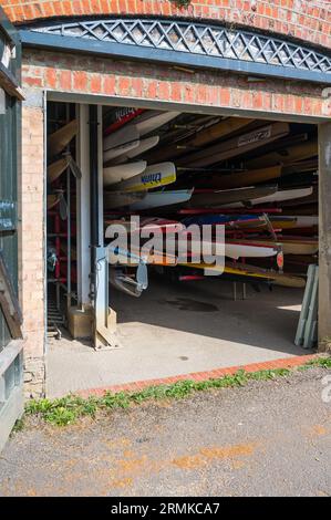 Vu à travers les portes ouvertes, une variété de canoës, kayaks et écules d'aviron entreposés dans le hall à bateaux du Richmond Canoe Club. Richmond, Londres, Angleterre, Royaume-Uni Banque D'Images