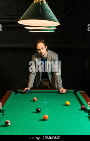 Jeune homme costume de billard debout piscine tenant club de balle Banque D'Images