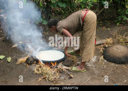 Femme cuisinant Injera (crêpe comme du pain) sur un mogogo au-dessus d'un feu dans la ville de marché de Jinka, vallée de l'Omo, Éthiopie Banque D'Images