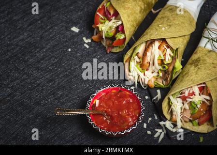 Tortillas végétaliennes maison avec haricots rouges, patates douces, tomates et guacamole avec sauces et épices sur fond noir. Banque D'Images