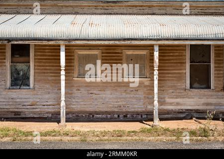 Une vieille maison de panneau d'étanchéité délavé et écaillé peint dans une ville rurale de Victoria Australie avec des fenêtres symétriques et un toit de patio ondulé Banque D'Images