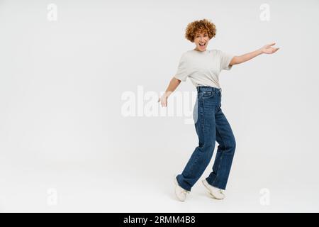 Femme bouclé de gingembre portant un t-shirt souriant et dansant isolé sur fond blanc Banque D'Images