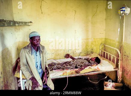 Mali, Dioila. Homme assis à côté de sa femme, qui est attaché à un goutte à goutte dans une clinique de village. Banque D'Images