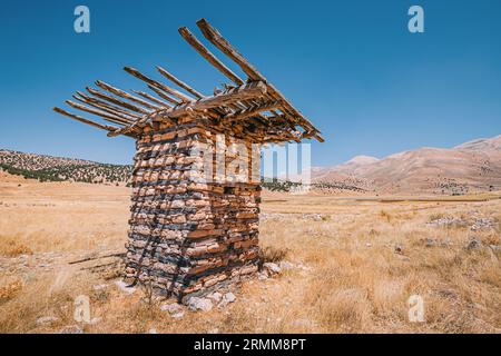 Une ancienne maison en pierre abandonnée ou une autre structure au milieu d'un paysage désertique, encadrée par des montagnes et un vaste ciel bleu. Banque D'Images