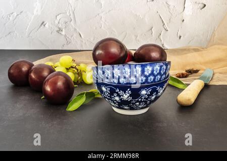 Une nature morte avec des prunes rouges mûres dans des bols en porcelaine bleue et un couteau pour les couper en deux et les manger Banque D'Images