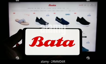 Personne tenant le smartphone avec le logo de la société de chaussures Bata Corporation sur l'écran en face du site Web. Concentrez-vous sur l'affichage du téléphone. Banque D'Images