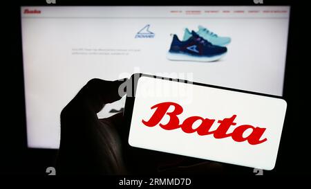 Personne tenant le téléphone portable avec le logo de la compagnie de chaussures Bata Corporation sur l'écran en face de la page Web d'affaires. Concentrez-vous sur l'affichage du téléphone. Banque D'Images