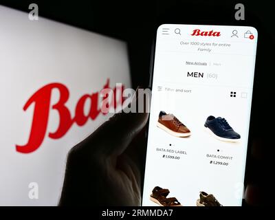 Personne tenant le téléphone portable avec la page Web de la compagnie de chaussures Bata Corporation sur l'écran devant le logo. Concentrez-vous sur le centre de l'écran du téléphone. Banque D'Images