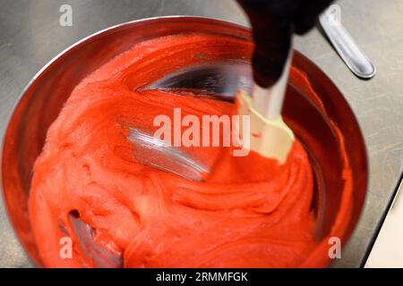 chef pâtissier styr crème au beurre rouge pour la décoration des gâteaux dans la cuisine professionnelle Banque D'Images