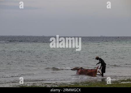 Pêcheur solitaire à la plage de sable du Mozambique préparant le bateau pour aller à la voile et à la pêche Banque D'Images