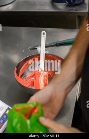 chef pâtissier styr crème au beurre rouge pour la décoration des gâteaux dans la cuisine professionnelle Banque D'Images