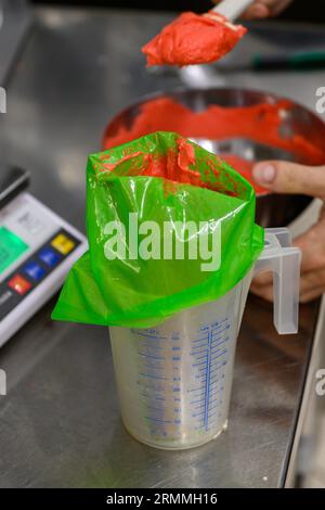 chef pâtissier styr crème au beurre rouge pour la décoration des gâteaux dans la cuisine professionnelle Banque D'Images