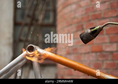 Utilisation d'un chalumeau pour enlever la peinture d'un cadre de vélo orange en cours de rénovation dans un atelier de vélo. Banque D'Images