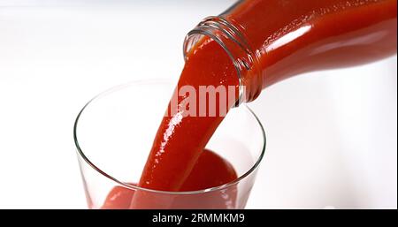 Le jus de tomatoe étant versé dans un verre sur fond blanc Banque D'Images