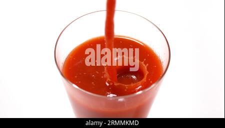 Le jus de tomatoe étant versé dans un verre sur fond blanc Banque D'Images