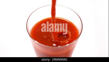 Le jus de tomatoe étant versé dans un verre sur fond blanc Banque D'Images