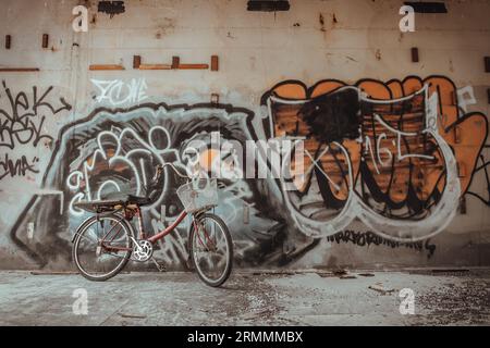 Bangkok, Thaïlande - 08 juillet 2023 - Un vélo rouge est garé à côté des motifs de graffiti sur le mur, dans le bâtiment abandonné. Espace pour le texte Banque D'Images