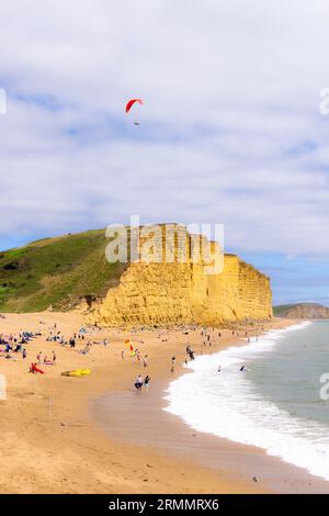 Un parapont parapontant sur la plage West Bay Dorset, plage et falaises, et les gens sur la plage en été ; West Bay, Dorset UK Banque D'Images